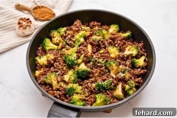 Sautéed ground beef with crisp tender broccoli tossed with sweet and savory sauce in sauté pan topped with sesame seeds.