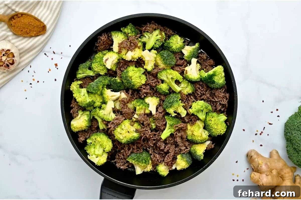 Browned beef in skillet with fresh broccoli florets and beef broth added in. pan