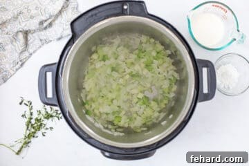 Softened diced yellow onions and celery inside inner pot of Instant Pot for base of Instant Pot Wild Rice Soup.