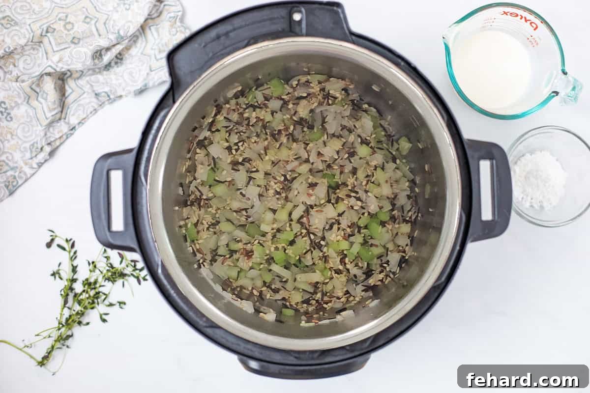 Onion, celery, wild rice, and minced garlic lightly sautéing and toasting together in the Instant Pot, preparing for the next steps of the creamy wild rice soup.