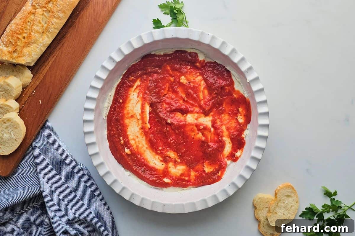 Pizza Dip Layered with Sauce Pizza dip base in a pie plate, freshly topped with an even layer of vibrant pizza sauce, ready for cheese and toppings.