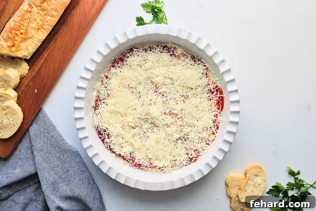 Pizza Dip with Mozzarella Pizza dip base and sauce layered with generous shredded mozzarella cheese, preparing for toppings.