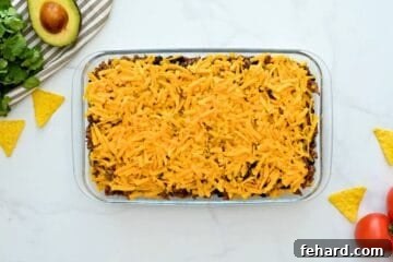 Corn chips, taco meat, beans, corn, and cheese layered in 7x11 baking dish before baking.