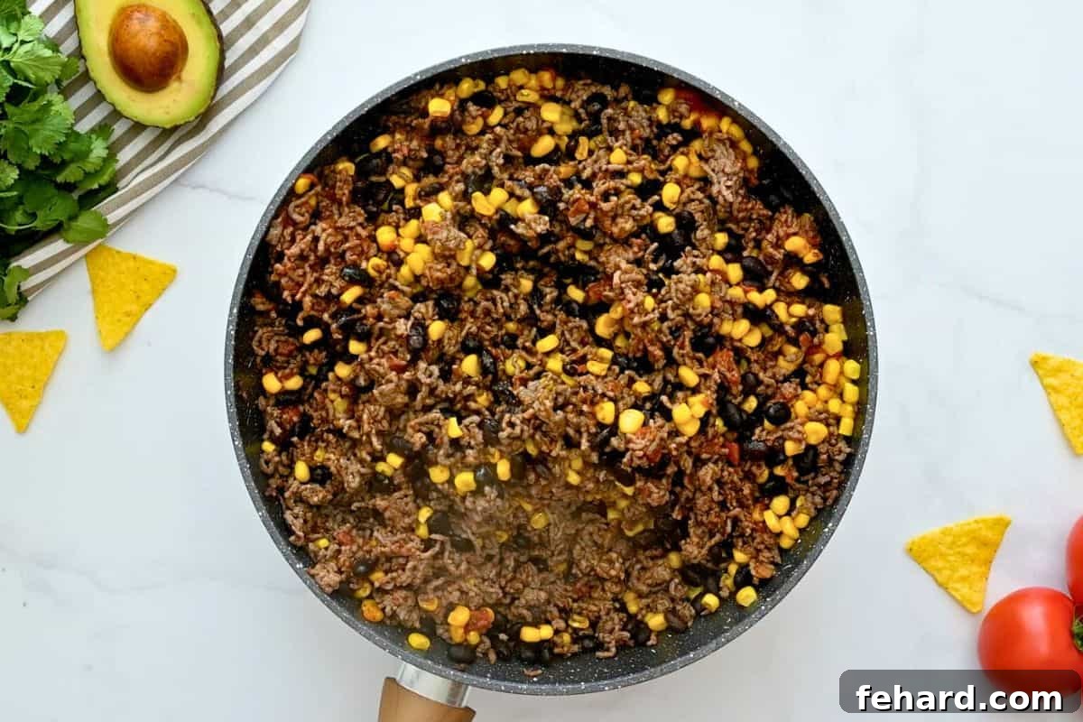 Mexican Taco Bake Casserole Filling A vibrant skillet filled with seasoned ground beef, a colorful blend of black beans and corn, simmered in rich tomato sauce and taco seasoning, ready to be layered into the casserole.