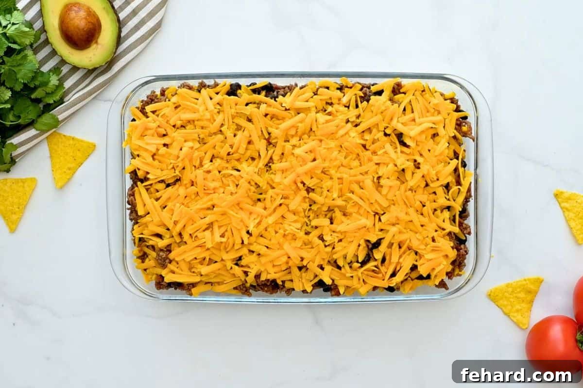 Easy Taco Casserole Assembly Layers of golden corn chips, savory taco meat, hearty beans, sweet corn, and shredded cheese beautifully arranged in a 7x11 baking dish, prepared for baking.