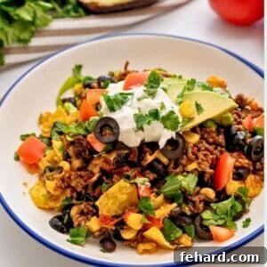 Plate of taco casserole made with ground beef and beans, cheese topped with lettuce, cilantro, tomatoes, and sour cream.