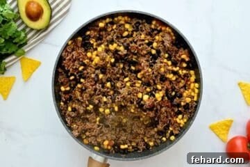 Ground beef, beans, and corn in large skillet seasoned with tomato sauce and taco seasoning to form base
