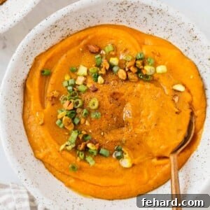 Close up of a bowl of carrot leek soup with green onions as garnish.