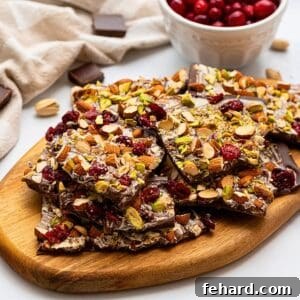 Chocolate bark on cutting board made with chopped nuts, dried cranberries, and sea salt.