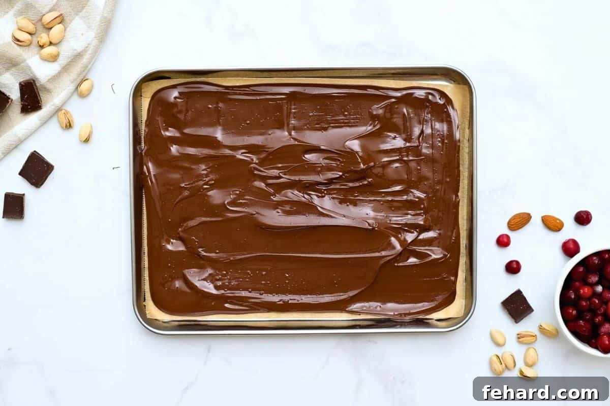 Smooth, melted dark chocolate evenly spread to a quarter-inch thickness on parchment paper, ready for the next delicious layers.
