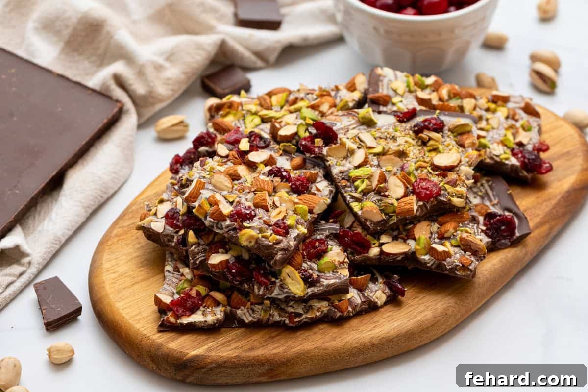 Irregularly broken pieces of delicious chocolate bark, adorned with chopped nuts, dried cranberries, and a sprinkle of sea salt, arranged on a rustic cutting board.
