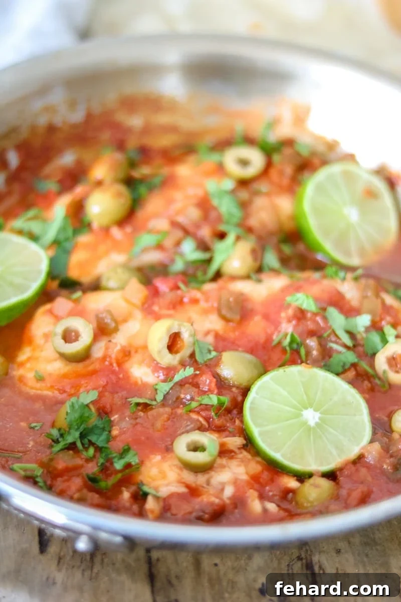 Cooked Fish Veracruz Ready to Serve Skillet with cooked tilapia in a rich Veracruz sauce, garnished with fresh lime and cilantro.