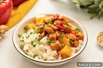 Instant Pot Sweet and Sour Chicken served with white rice in white bowl next to fresh pineapple and peppers.