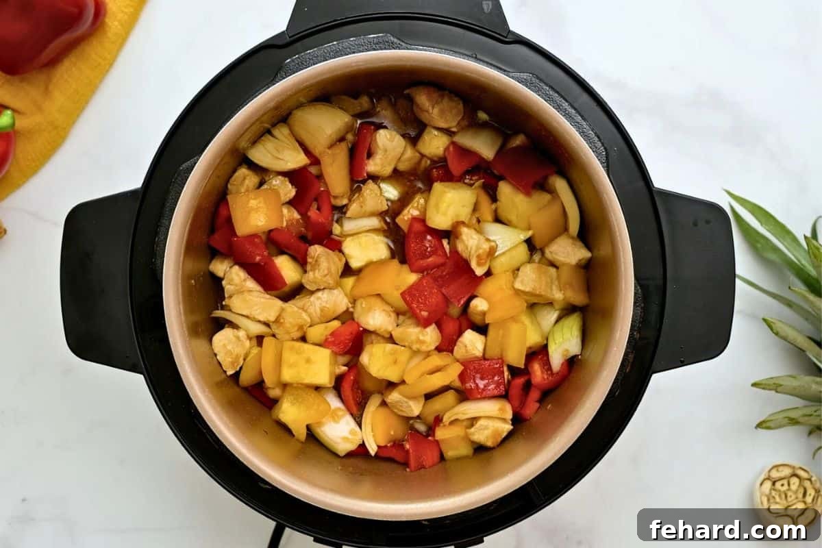 Chicken, pineapple, peppers, and onions layered with homemade sweet and sour sauce inside the Instant Pot, ready for cooking.