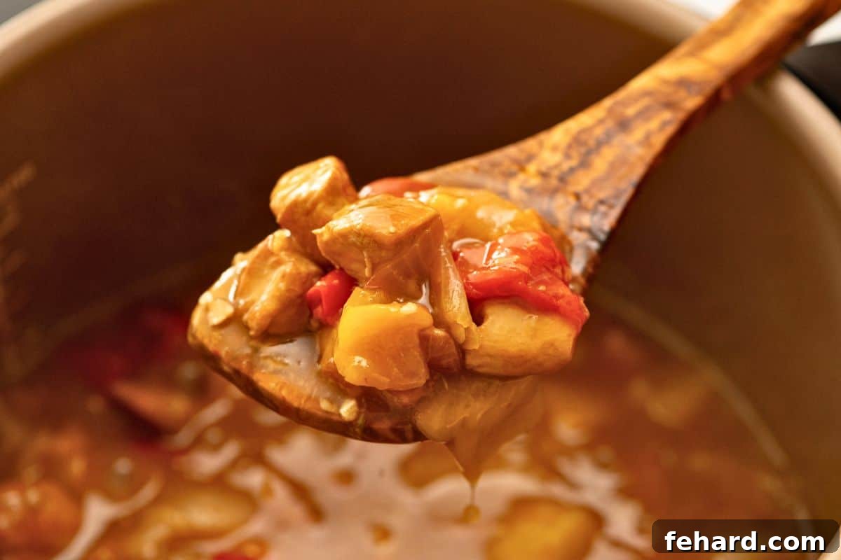 A spoonful of thickened Instant Pot Sweet and Sour Chicken with peppers and pineapple, showing the perfect sauce consistency after simmering.