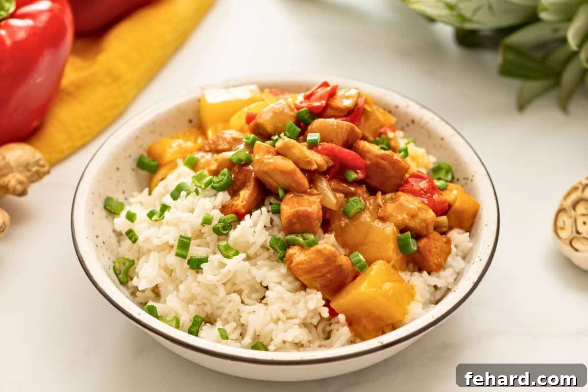 A perfectly plated dish of Instant Pot Sweet and Sour Chicken with white rice, accompanied by fresh pineapple chunks and bell pepper slices.