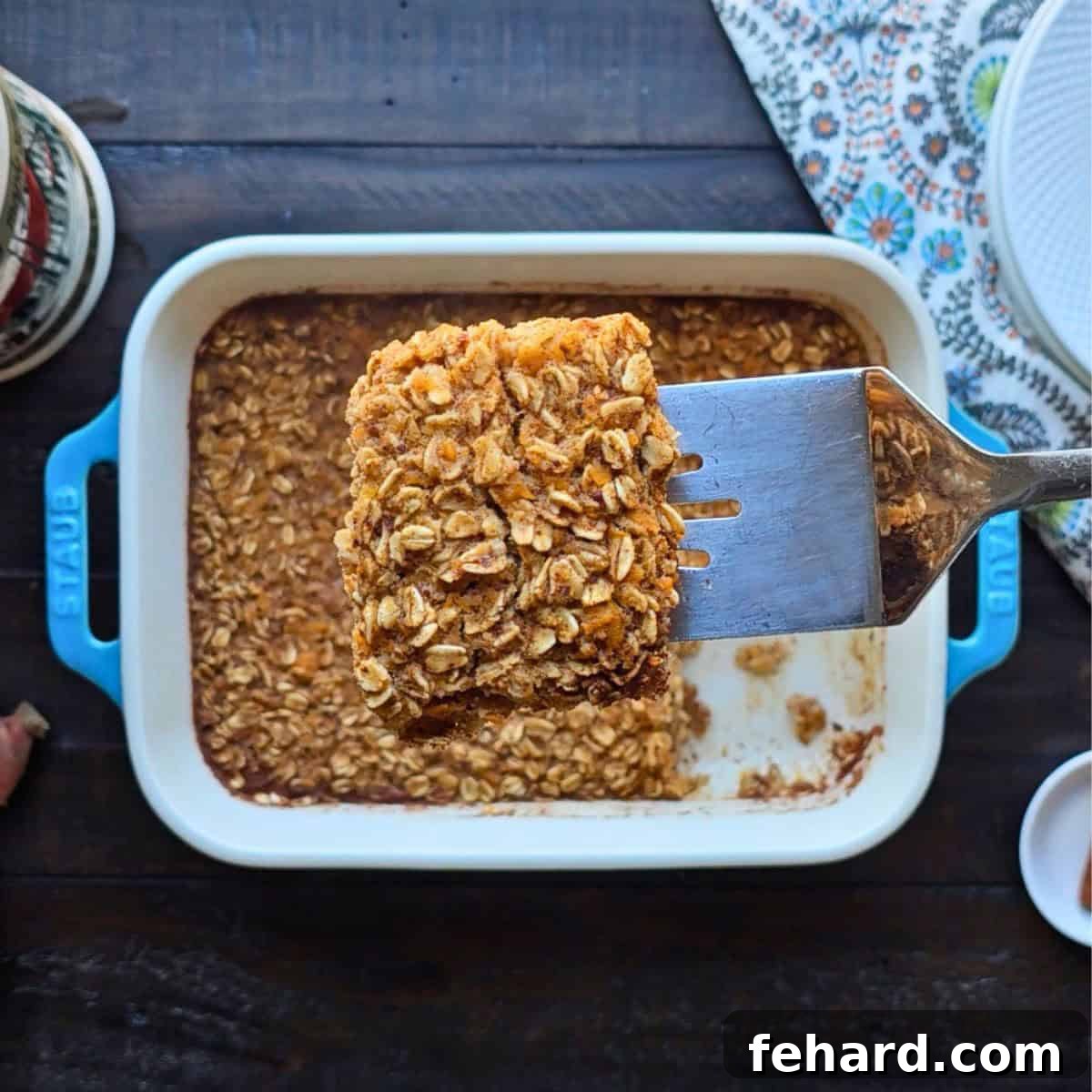 Spatula lifting out slice of sweet potato baked oatmeal from blue staub baking dish.