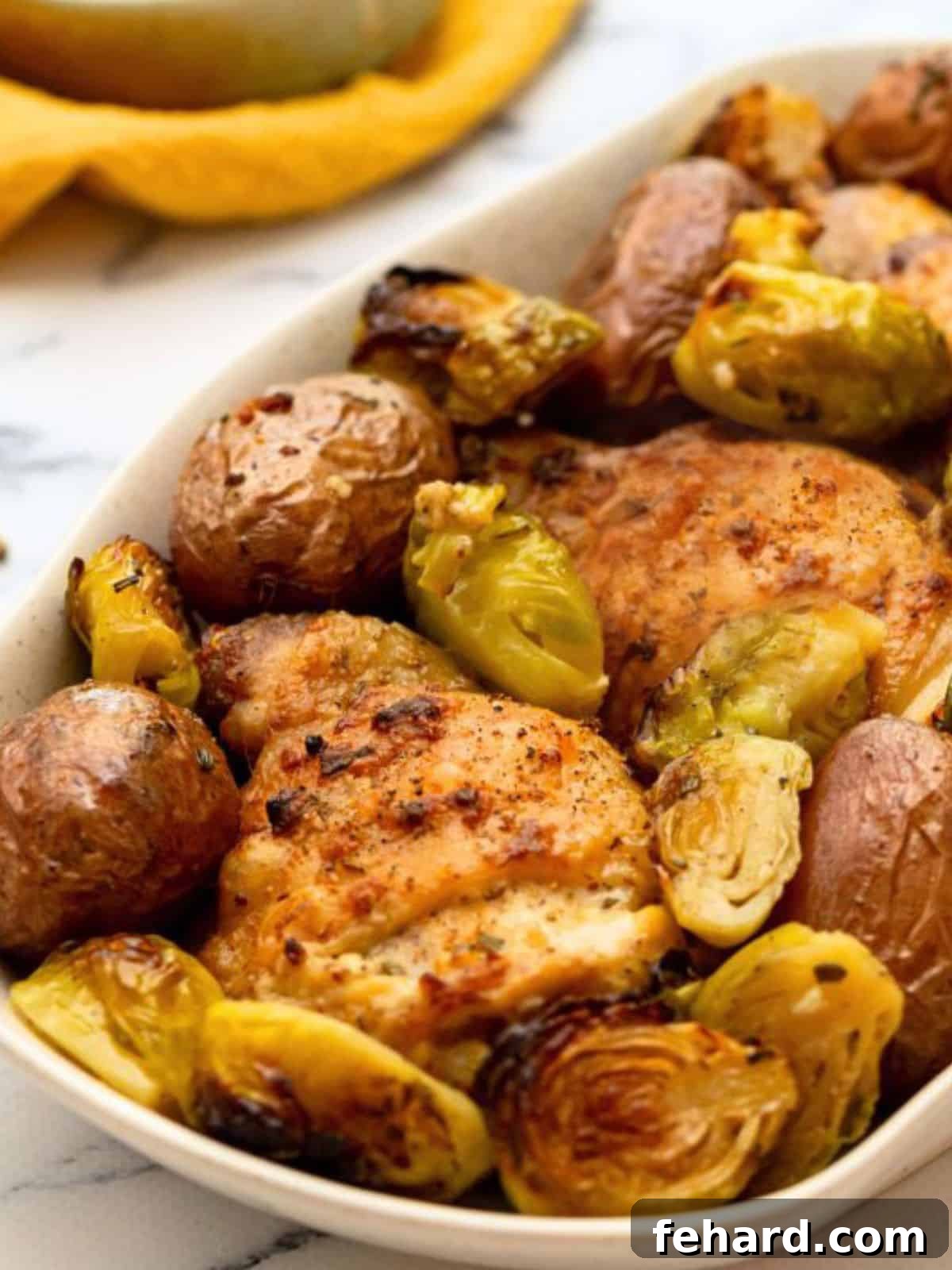 Sheet pan chicken thighs with potatoes and vegetables plated on white dish. A perfectly roasted, wholesome, and easy family meal ready in under an hour.