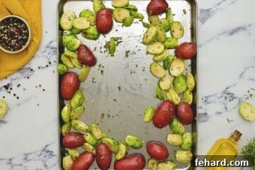 Red baby potatoes and brussel sprouts seasoned and spread out on rimmed sheet pan for chicken thigh sheet pan dinner.