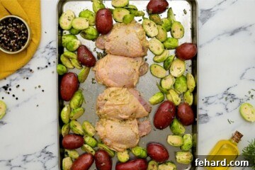 Seasoned Chicken Thighs, potatoes, and brussels sprouts spread out on sheet pan.