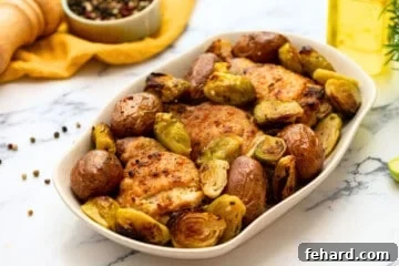 Sheet pan chicken thighs with potatoes and vegetables on white dish.
