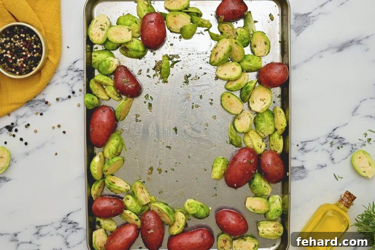 Red baby potatoes and brussel sprouts seasoned and spread out on rimmed sheet pan for chicken thigh sheet pan dinner. Ready for roasting with other ingredients.