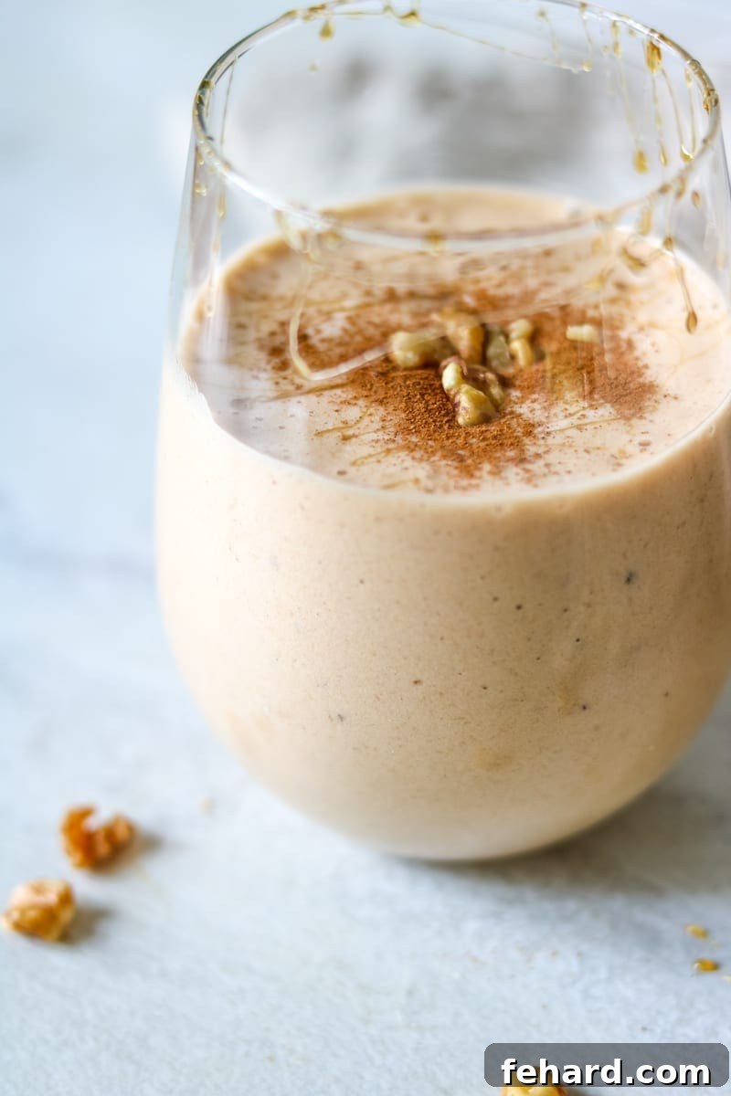 A vibrant and delicious Vegan Sweet Potato Pie Smoothie served in a clear glass, beautifully garnished with a sprinkle of warming cinnamon, a drizzle of sweet maple syrup, and crunchy chopped walnuts. Perfect for a healthy breakfast or an energizing snack.