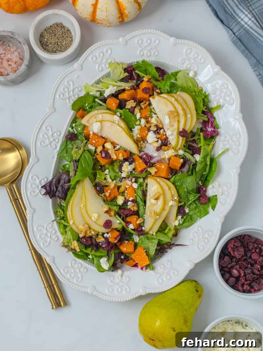 A large white platter presenting a beautiful fall salad with mixed greens, roasted butternut squash cubes, thinly sliced pears, scattered dried cranberries, crumbled feta cheese, and a drizzle of apple cider vinaigrette.