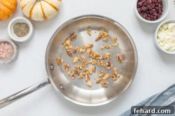 Toasted walnuts inside small stainless steel pan next to feta and dried cranberries for fall salad.