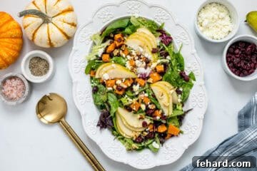 Salad served on white platter with mixed greens, pears, dried cranberries, roasted butternut squash, and apple cider vinaigrette.