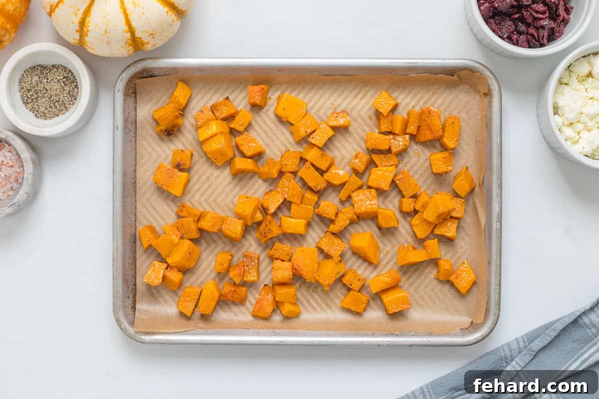 Roasted cubed butternut squash pieces spread evenly on a baking sheet lined with parchment paper, golden and caramelized around the edges, ready for cooling.