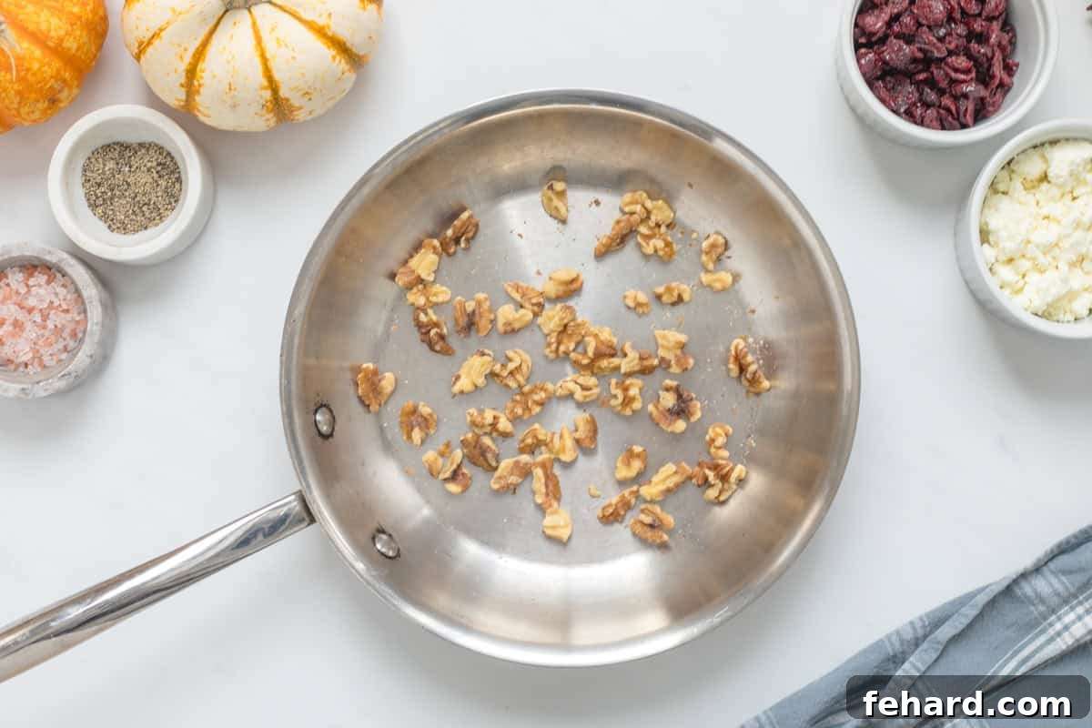 A small stainless steel pan containing freshly toasted walnuts, alongside small piles of crumbled feta cheese and vibrant dried cranberries, all components for the delightful fall salad.