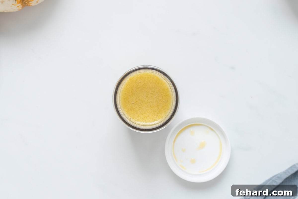 A small ball jar filled with a golden apple cider vinaigrette, ready to be drizzled over a fresh fall salad.