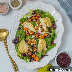 Fall salad on large white platter made with mixed greens, roasted butternut squash, sliced pears, toasted walnuts, dried cranberries, feta, and apple cider vinaigrette.