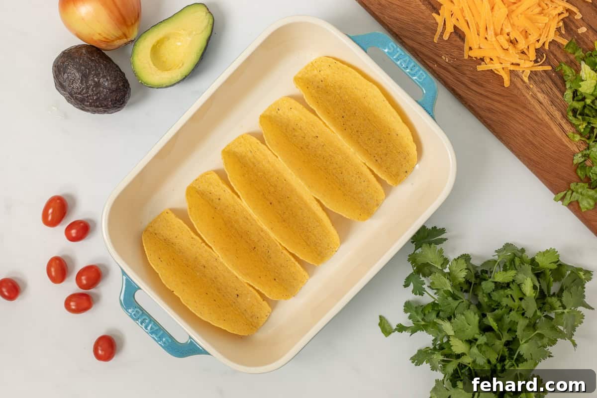 Crispy hard taco shells neatly arranged in a baking dish, ready to be filled, alongside fresh cilantro, creamy avocado, and shredded cheese. This image highlights the preparation stage of making easy black bean tacos.