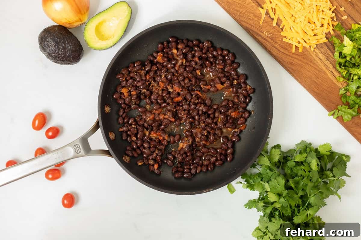 A close-up shot of black beans simmering in a sauté pan with salsa, creating a rich, flavorful filling for tacos. The image captures the bean mixture at its peak, ready for the final touches.