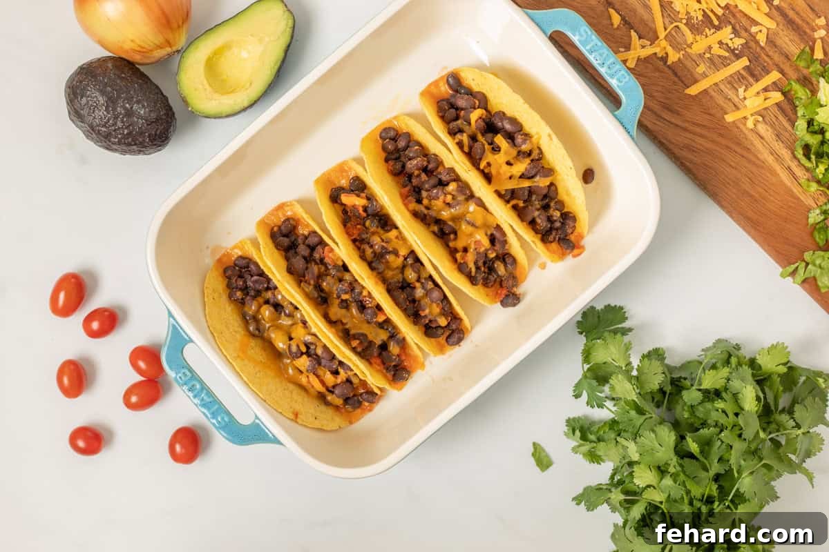 Toasted hard taco shells filled with a hearty black bean mixture and topped with shredded cheese, melting to golden perfection in the oven. This image showcases the final baking stage before serving.