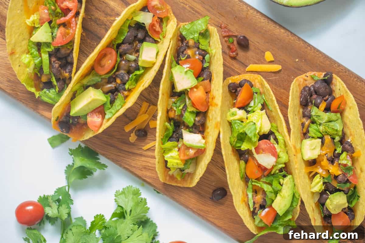 Beautifully assembled Black Bean Tacos displayed on a wooden cutting board, garnished with vibrant fresh toppings like chopped tomatoes, crisp green lettuce, cilantro, and slices of creamy avocado. A picture of a ready-to-eat healthy taco meal.
