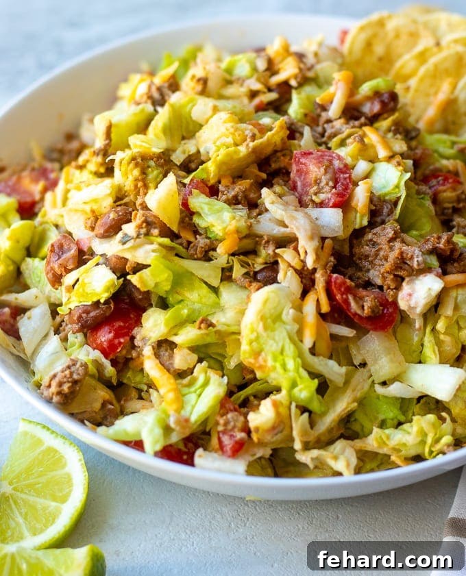 Assembled Homemade Taco Salad A large white bowl filled with a beautifully mixed homemade taco salad, featuring seasoned ground beef, fresh lettuce, diced tomatoes, onions, creamy avocado, and shredded cheese, all tossed together and ready to serve.