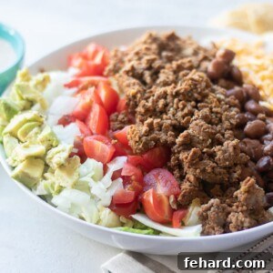 Taco Salad in white bowl with avocado, onion, tomatoes and ground beef