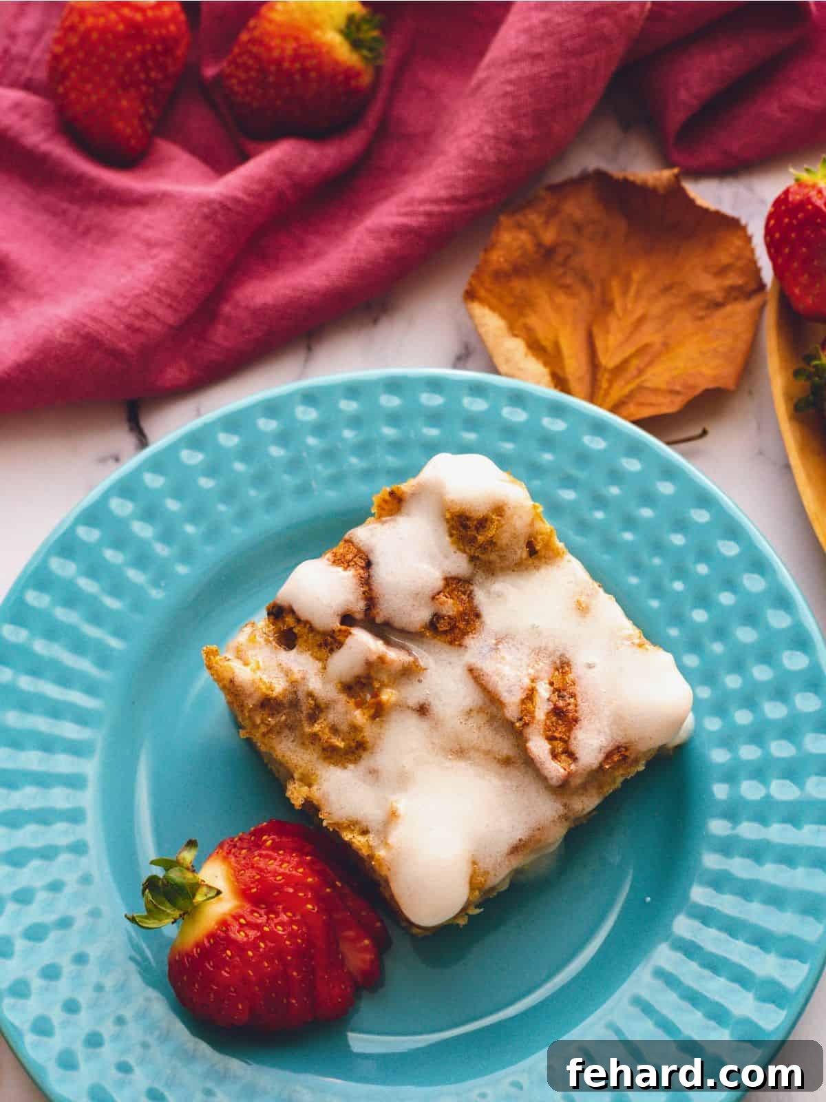 A beautifully presented slice of Overnight French Toast Casserole on a blue plate, drizzled with vanilla glaze and garnished with fresh strawberries.