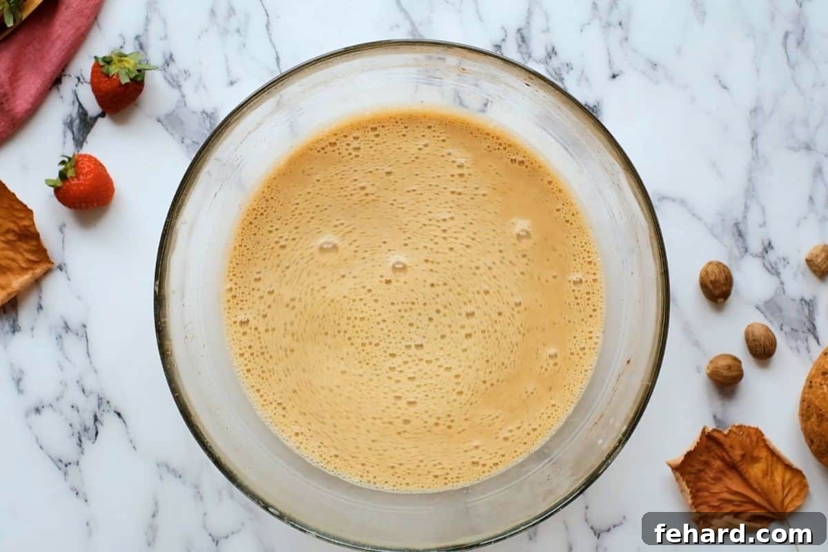 A mixing bowl showcasing the harmonious blend of eggs, rich maple syrup, warm cinnamon, fragrant nutmeg, and sweet vanilla extract, perfectly combined for the French toast custard.