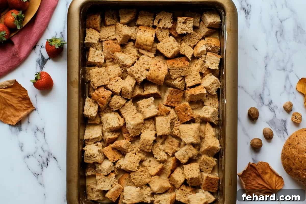Bread cubes generously soaked in a rich maple egg custard, nestled in a buttered baking dish, ready for an overnight chill to absorb all the delicious flavors.