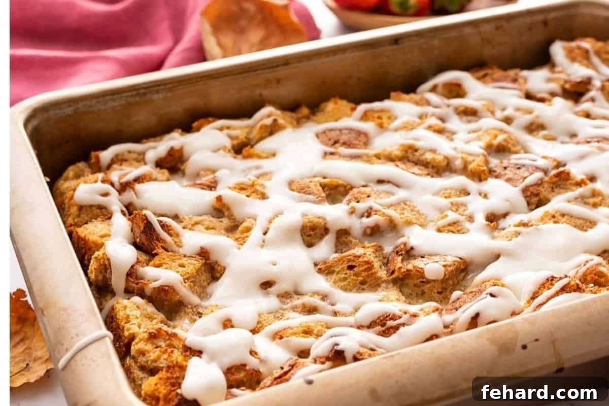 A close-up shot of the golden-baked French Toast Casserole in its baking dish, generously drizzled with a smooth, sweet vanilla glaze, highlighting its tempting appearance.