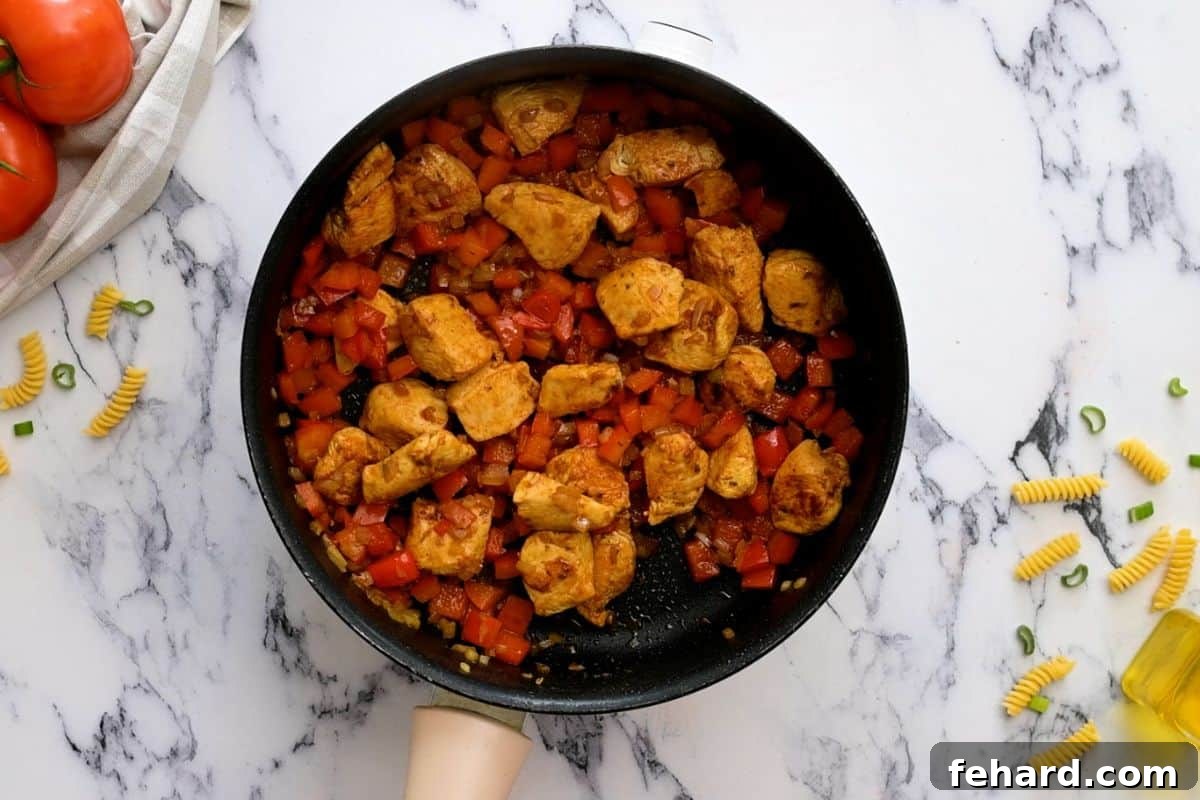 Sizzling skillet containing beautifully browned Cajun-spiced chicken, softened onions, and vibrant red bell peppers, creating an aromatic base.