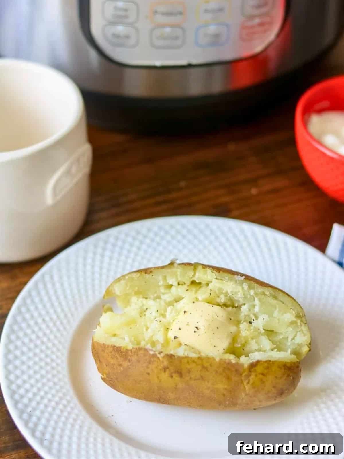 A perfectly baked Instant Pot potato on a white plate, generously topped with a dollop of melting butter, fresh cracked black pepper, and a sprinkle of sea salt. The potato's skin is slightly textured, hinting at a wonderfully fluffy and tender interior, ready to be enjoyed as a comforting side dish.