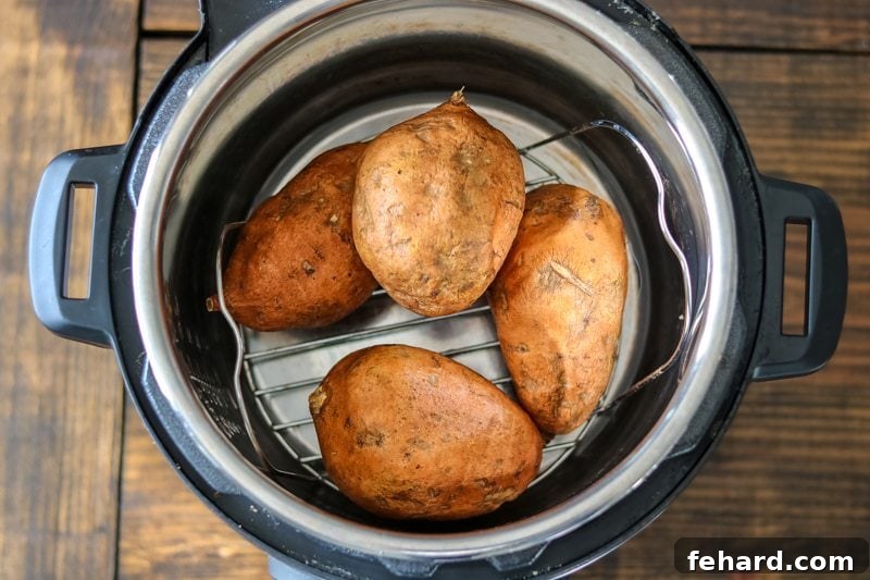 Raw sweet potatoes neatly stacked on a metal trivet inside an Instant Pot's inner pot, ready for pressure cooking.