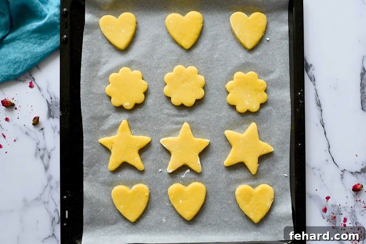 Heart, star, and flower cut-out sugar cookie dough perfectly spaced on a parchment-lined baking sheet, awaiting baking.