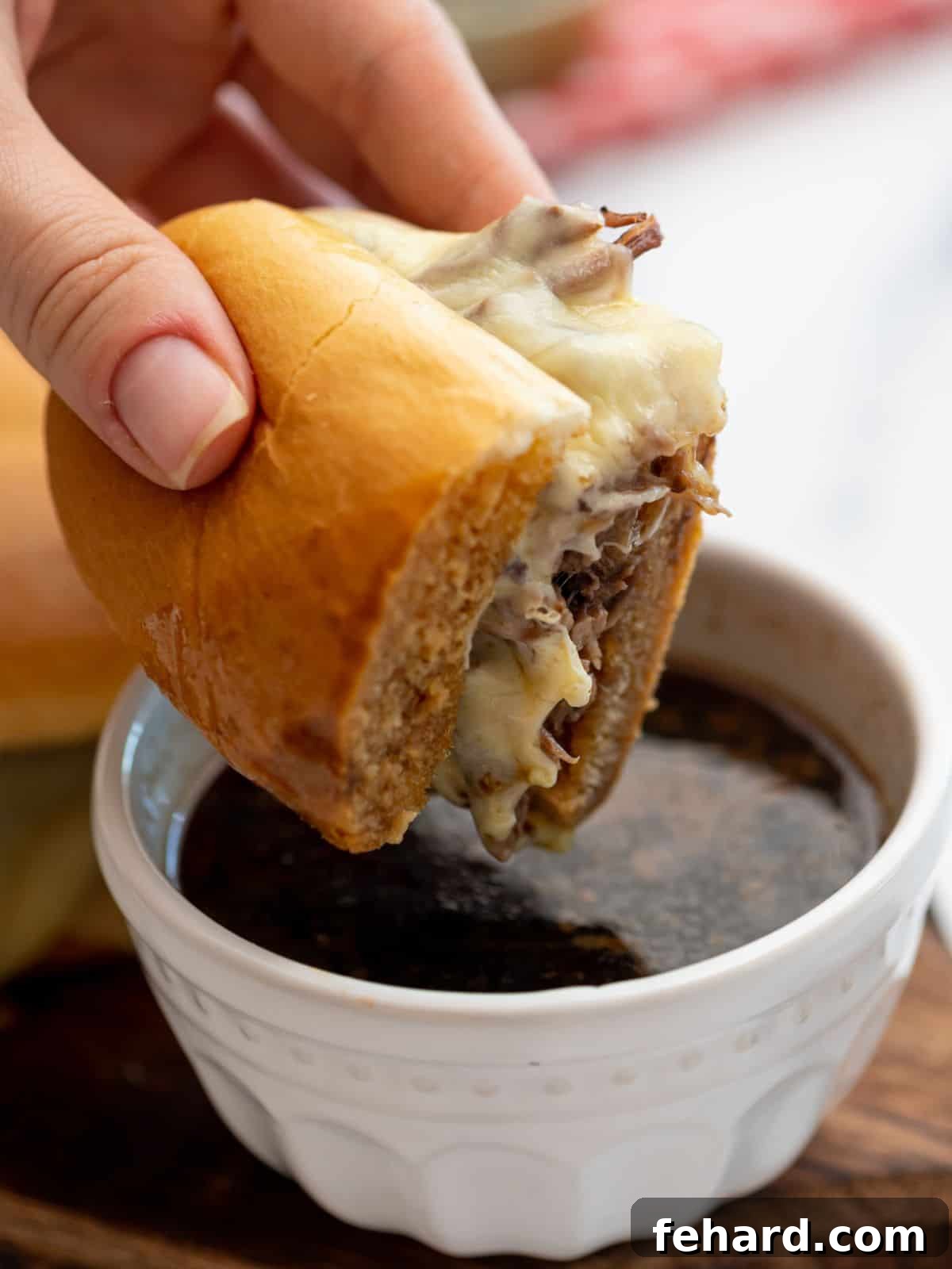A delicious Instant Pot French Dip sandwich, made with shredded beef and melted cheese, being dipped into a rich au jus.