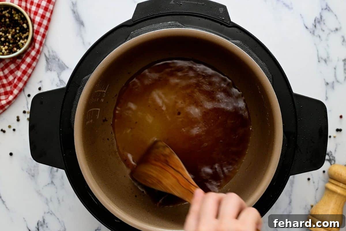 A wooden spatula scraping the bottom of the Instant Pot's inner pot to deglaze it, after searing beef.